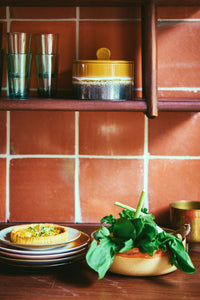 Kitchen scene with a shelf, tiled wall, and food items on a counter.