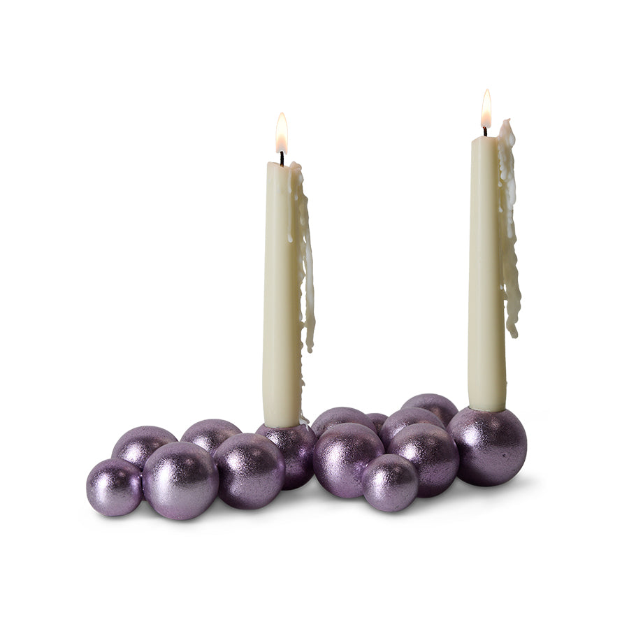 Two lit candles surrounded by purple decorative balls on a white background