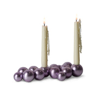 Two lit candles surrounded by purple decorative balls on a white background