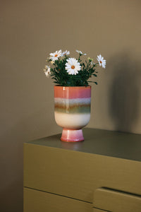 Multicolored vase with flowers on a green surface against a brown wall