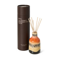 Ceramic diffuser bottle with fragrance sticks and brown cylindrical packaging on a white background