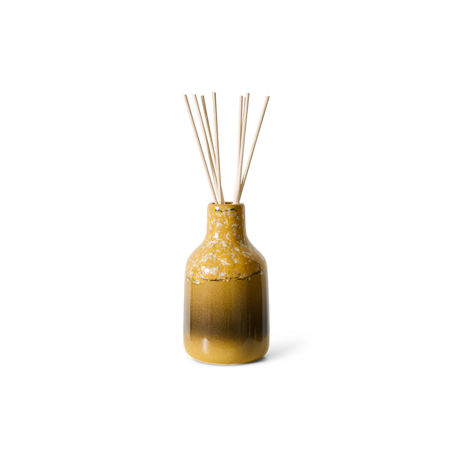 yellow and brown ceramic vessel with reeds diffuser on white background