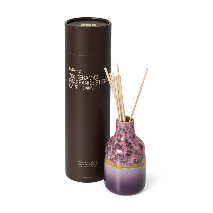 Pink ceramic diffuser with reeds and black cylindrical packaging on a white background
