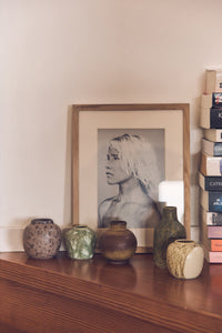 Framed portrait on a wooden shelf with decorative vases and books.