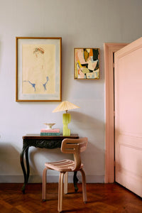 Room interior with a small table, chair, lamp, and framed artwork on a wall.