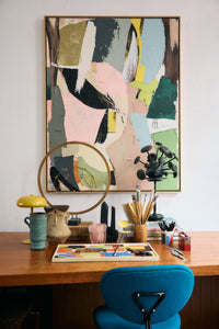 Colorful abstract painting above a desk with art supplies and a blue chair.