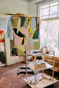 Art studio with abstract painting on an easel and a cart with supplies.