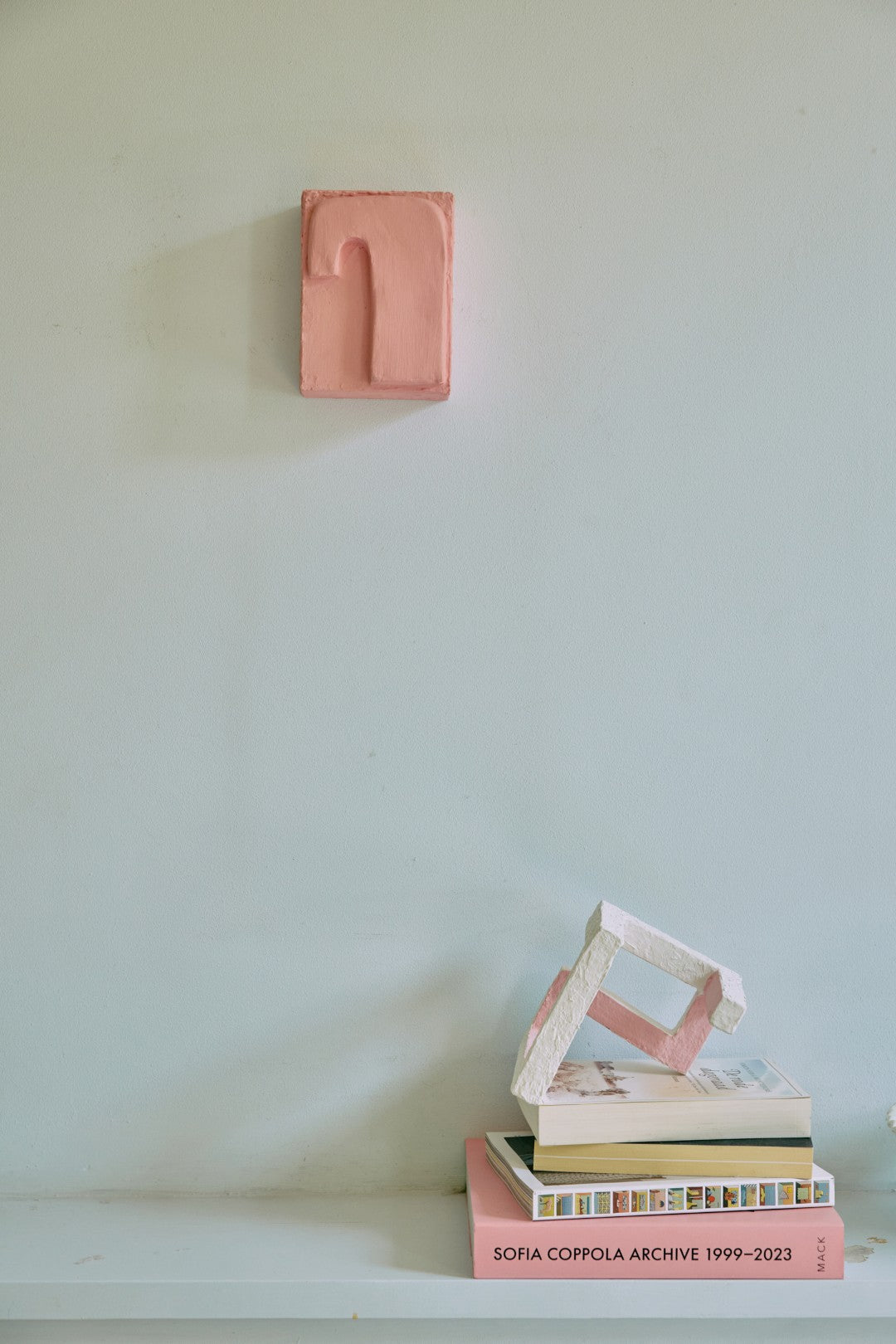 Stack of books with a pink rectangular object on a light surface against a white wall.