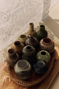 Collection of ceramic vases on a woven tray with a textured white background