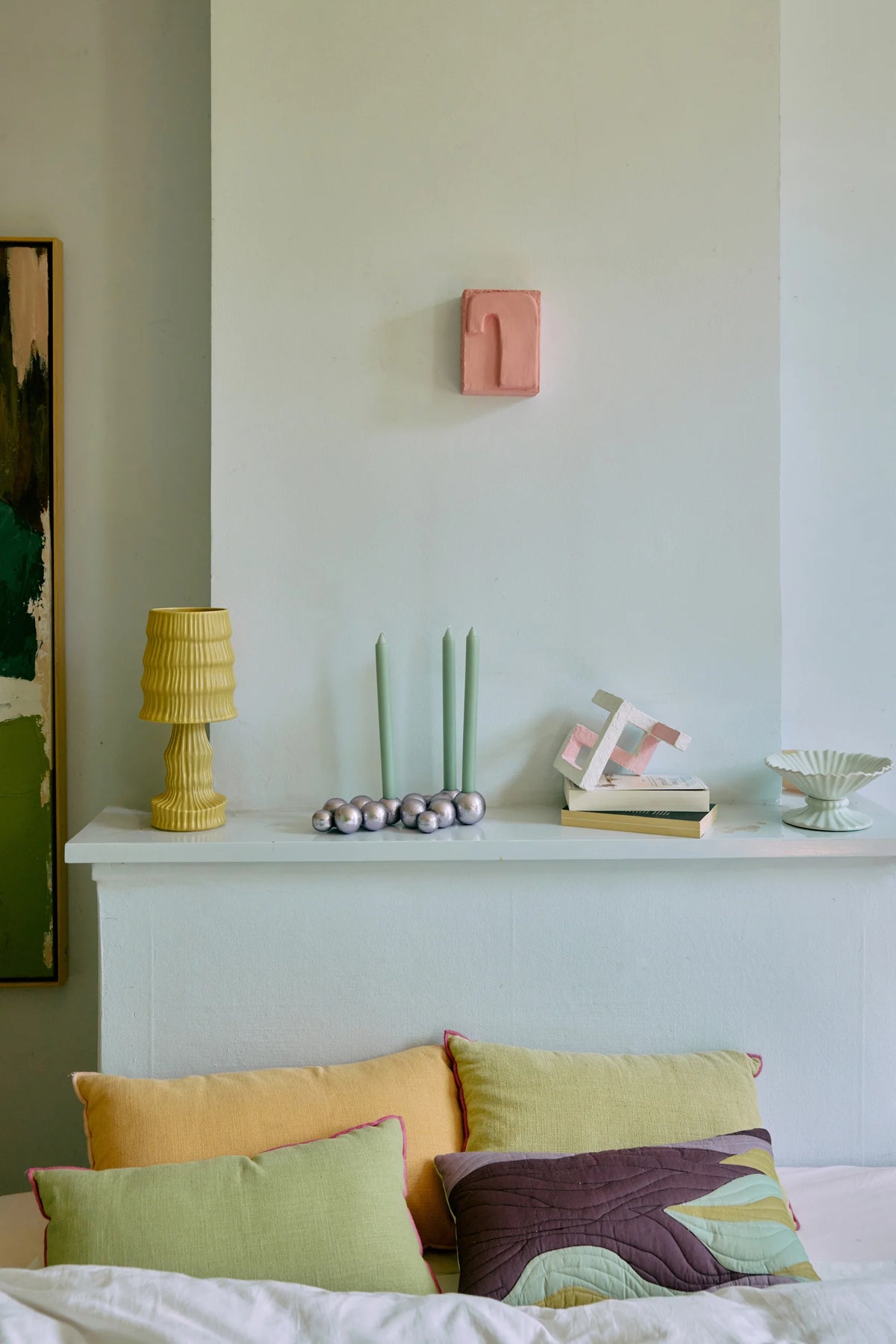 Decorative pillows on a bed with a lamp and small sculptures on a shelf in the background.