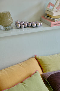 Section of a room with a white shelf, decorative items, and a yellow sofa with cushions.