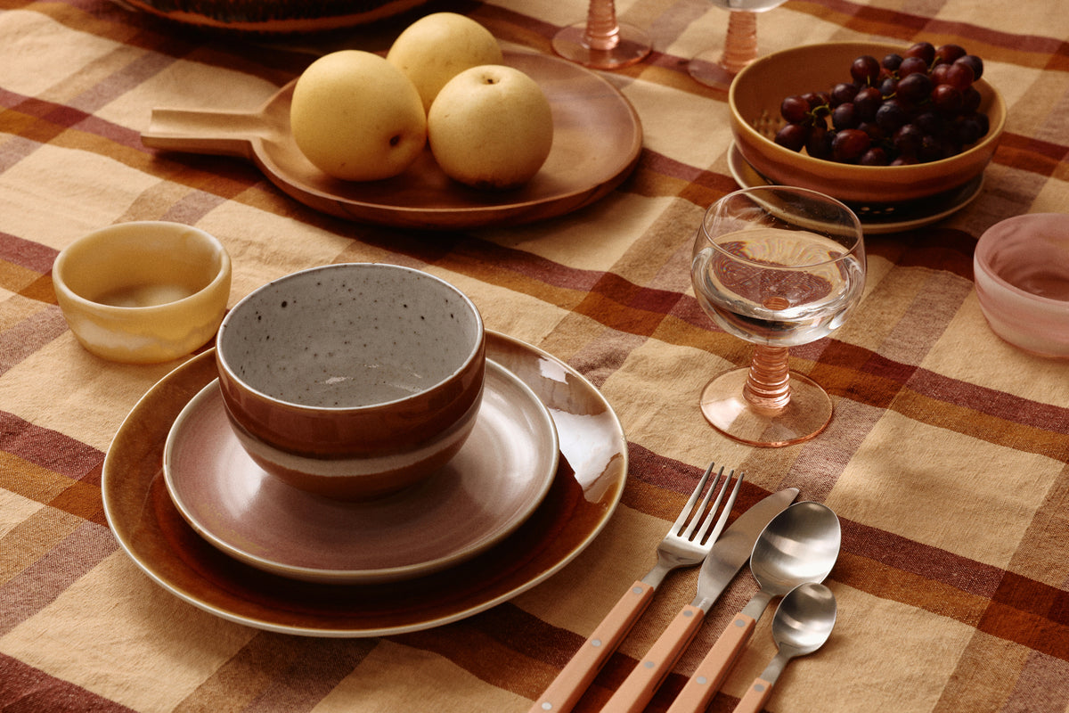 Dining table setting with plates, bowls, and cutlery on a checkered tablecloth.