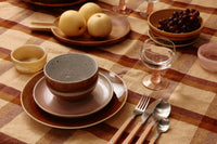 Dining table setting with plates, bowls, and cutlery on a checkered tablecloth.