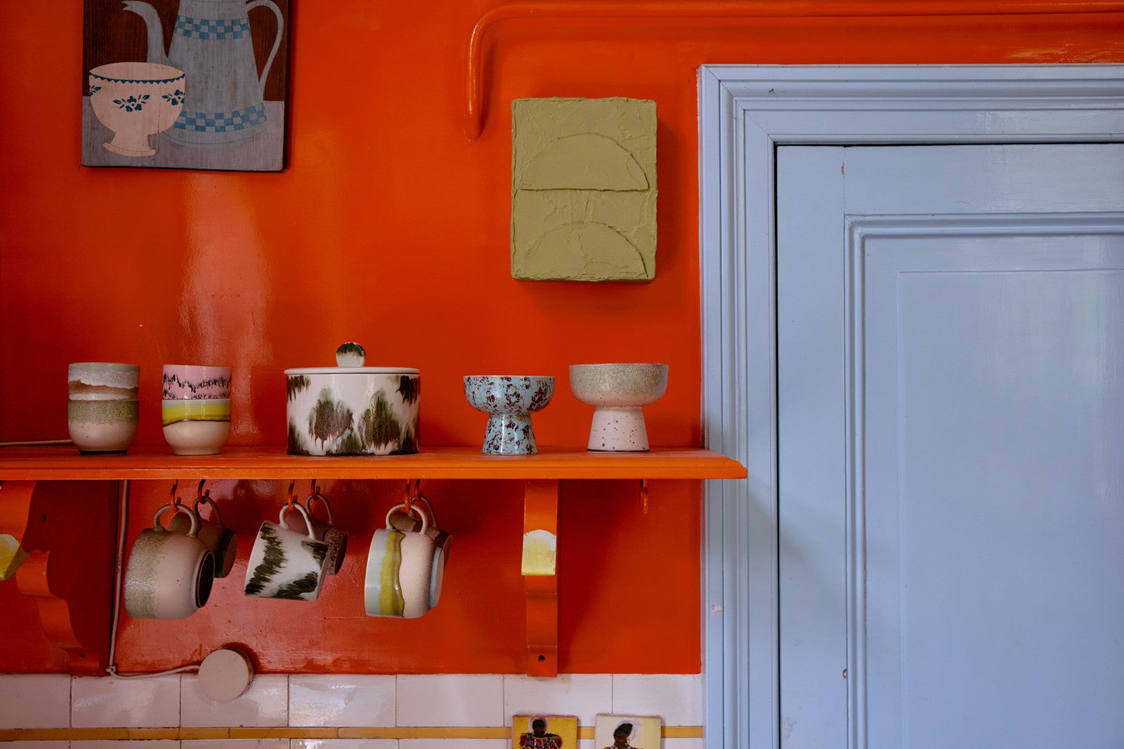 Orange wall with shelves displaying various ceramic items and a light blue door.