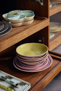 Stacked ceramic plates on a wooden shelf with a glass cabinet in the background.
