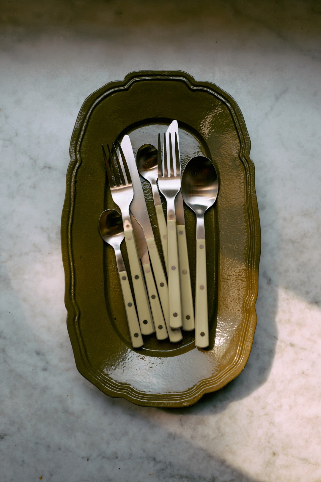 Set of silverware on a decorative green plate with a marble background
