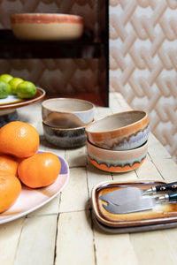 Ceramic bowls and a plate with oranges on a wooden surface.