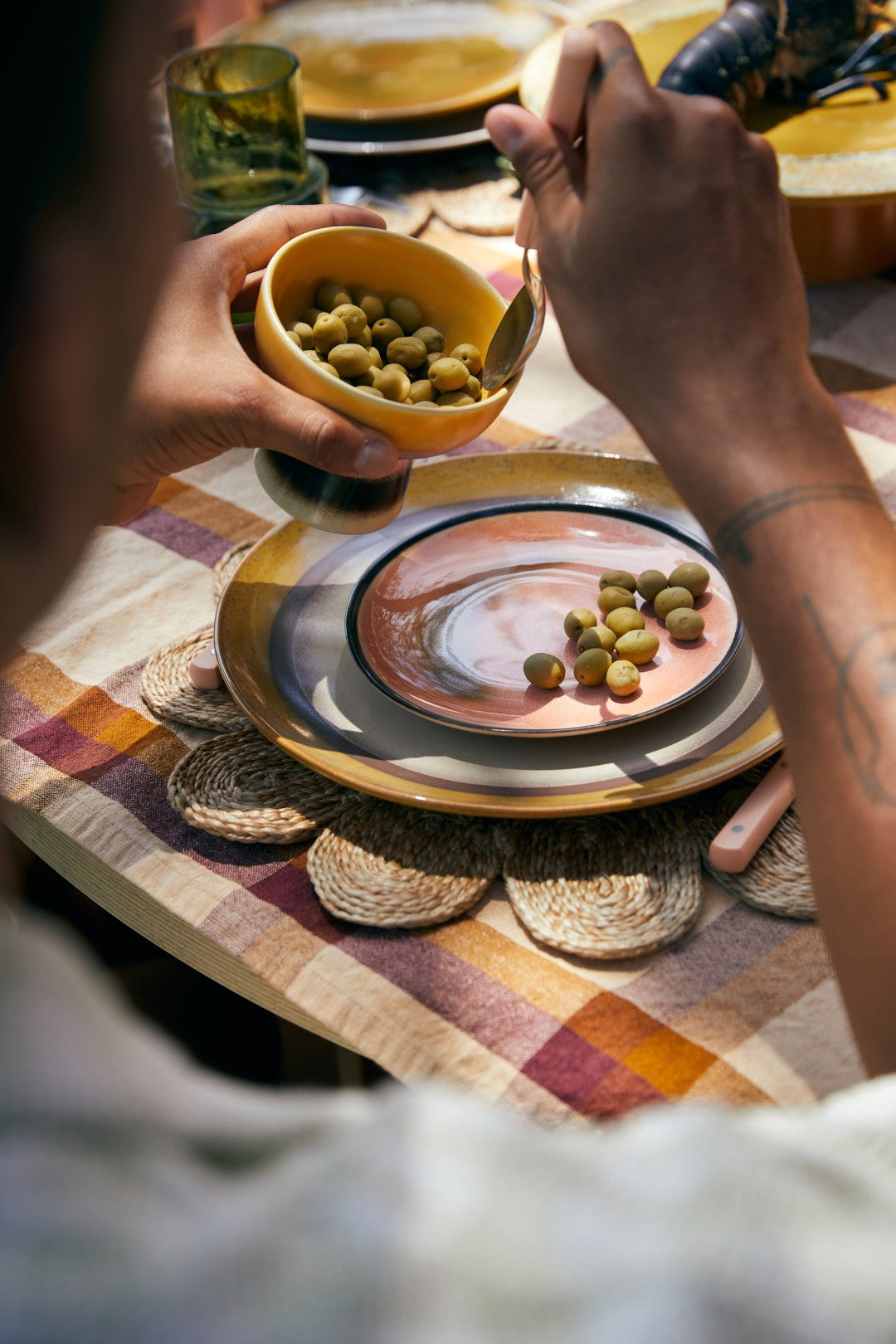 Person holding a bowl of olives over a plate with a colorful tablecloth.