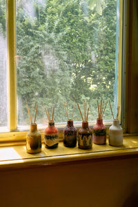 Set of diffuser bottles with sticks on a windowsill with a view of trees outside.