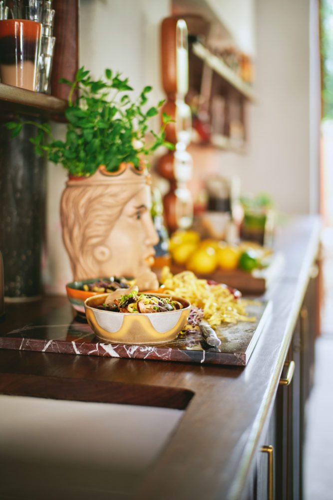 Kitchen counter with a bowl of food, a vase with plants, and lemons on a marble slab.