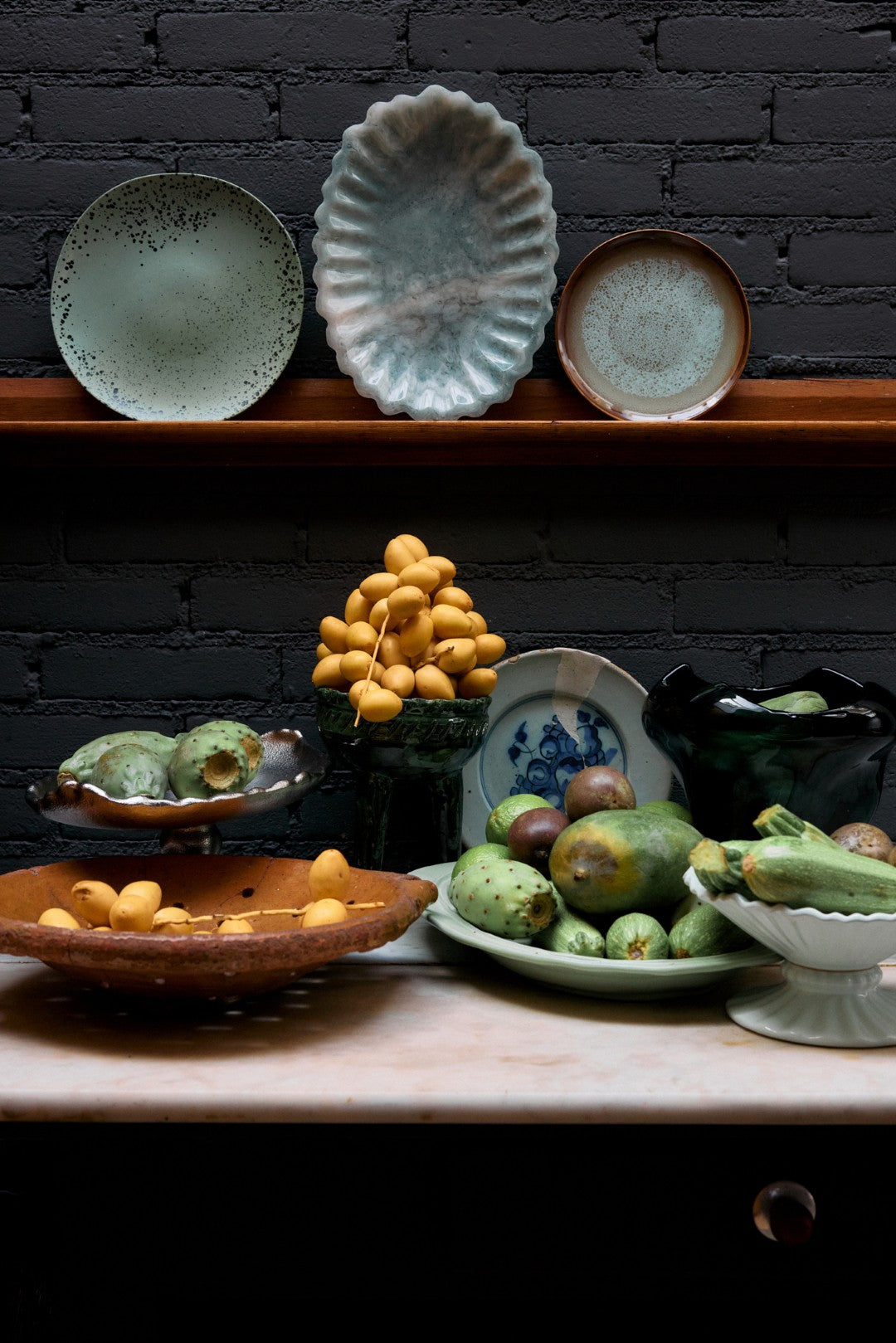 Decorative display of fruits and ceramic plates against a dark brick wall.