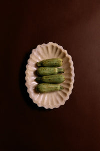 Four green zucchinis on a decorative white plate against a brown background