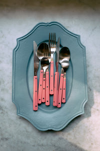 Set of silverware with pink handles on a decorative blue plate against a marble background