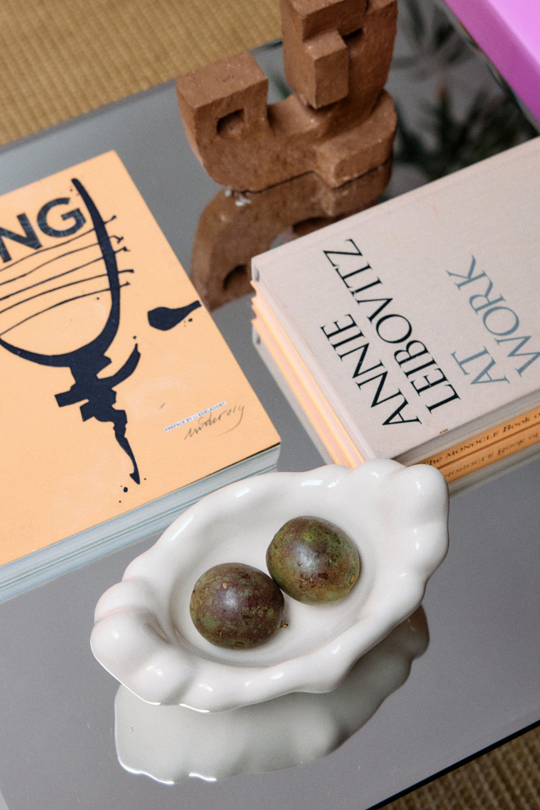 Small white dish with two green fruits on a reflective surface with books in the background