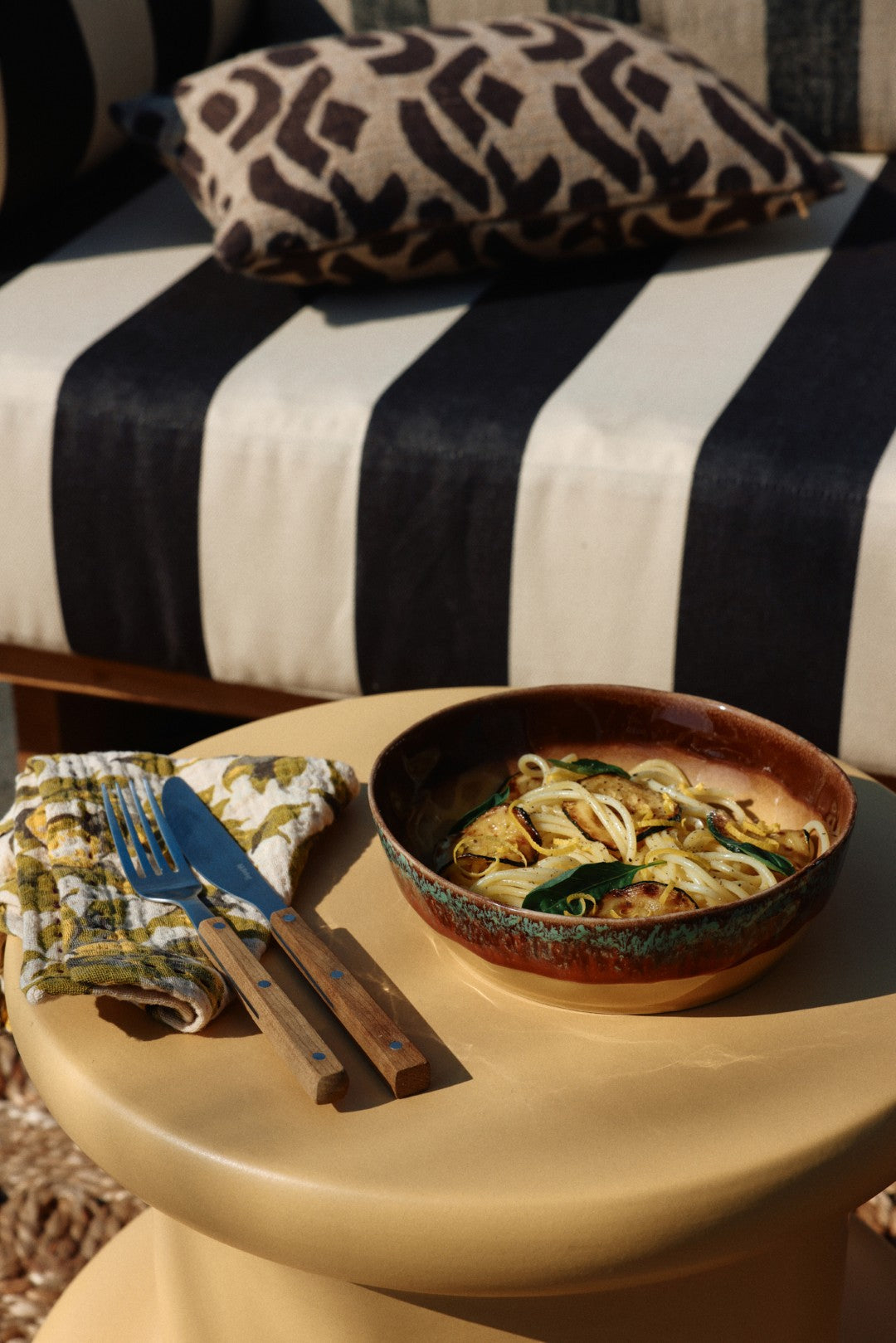 Bowl of pasta on a table with a striped chair in the background