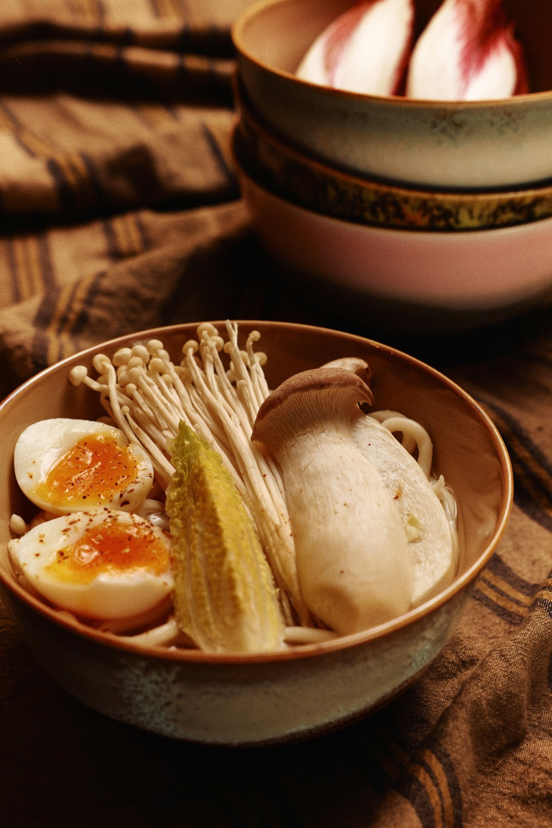 Bowl of noodles with vegetables and a soft-boiled egg on a patterned cloth.