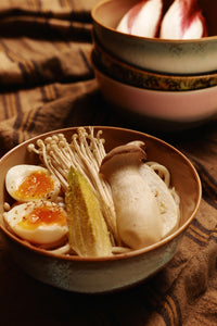 Bowl of noodles with vegetables and a soft-boiled egg on a patterned cloth.