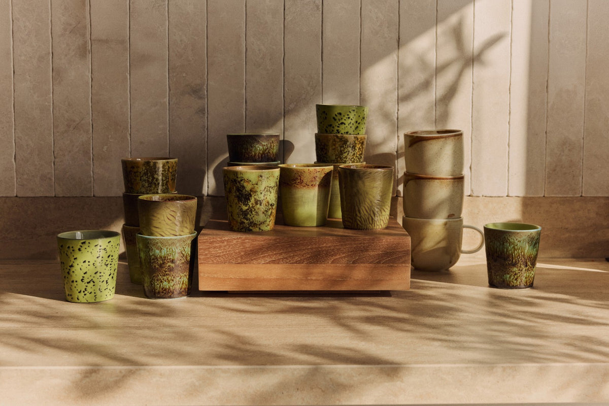 Collection of green ceramic cups on a wooden block against a neutral wall.