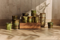 Collection of green ceramic cups on a wooden block against a neutral wall.