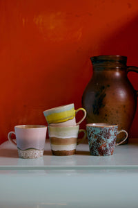 Set of ceramic mugs and a pitcher on a white surface with an orange wall background
