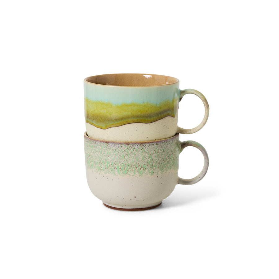 Two stacked ceramic mugs with green and beige glaze on a white background
