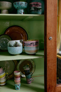 Collection of ceramic bowls and mugs on a green shelf with a wooden door partially open.