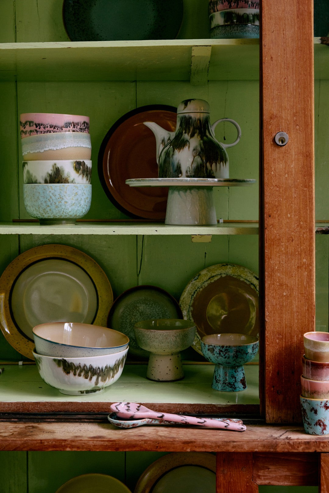 Collection of ceramic dishes and teapots on a wooden shelf against a green wall.