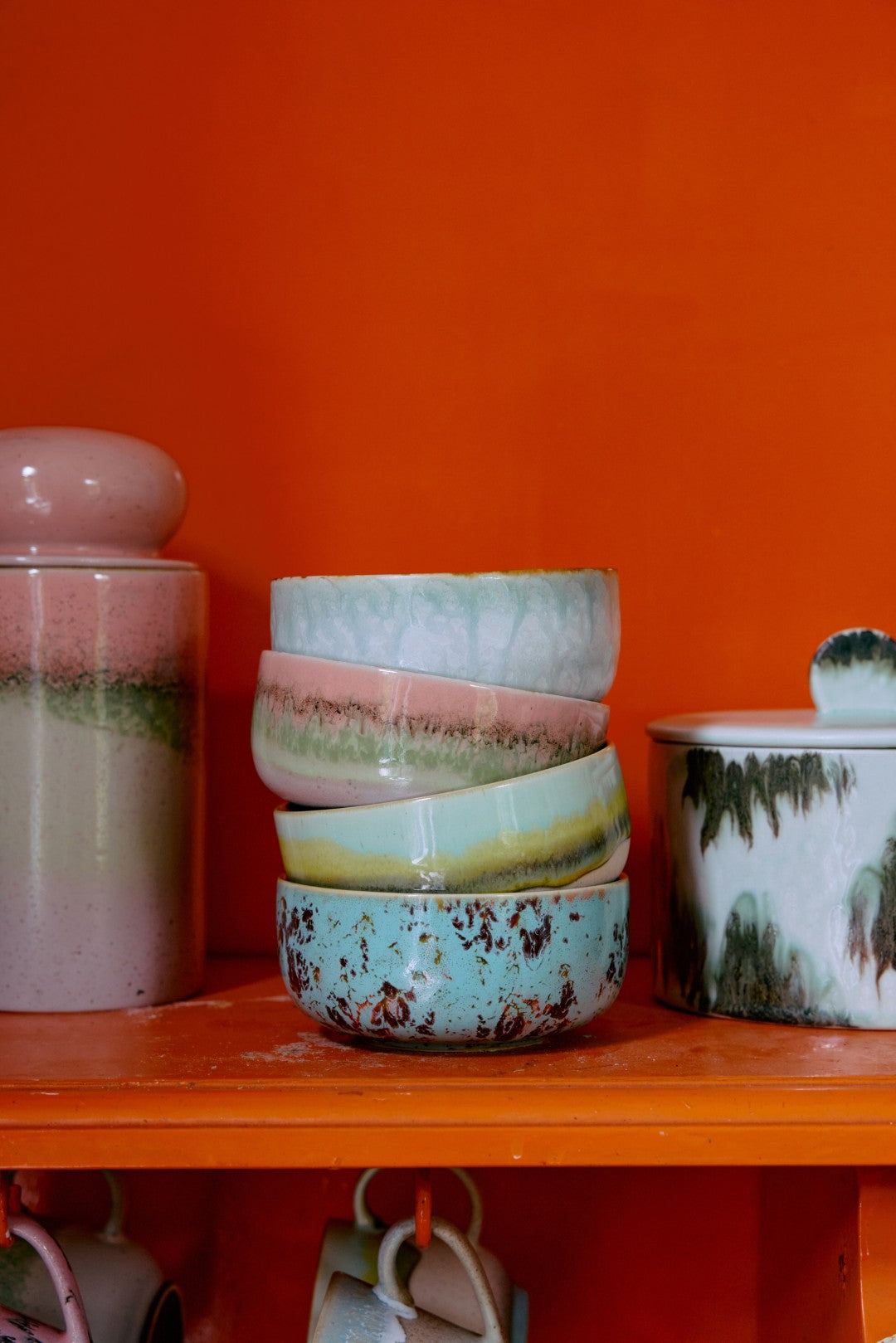 Stack of ceramic bowls with a colorful glaze on an orange shelf against an orange wall.