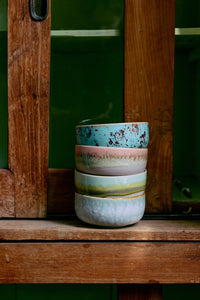 Stack of colorful ceramic cups on a wooden surface with a blurred green background