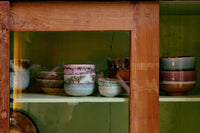 Collection of ceramic bowls on a shelf with a wooden frame and green wall background
