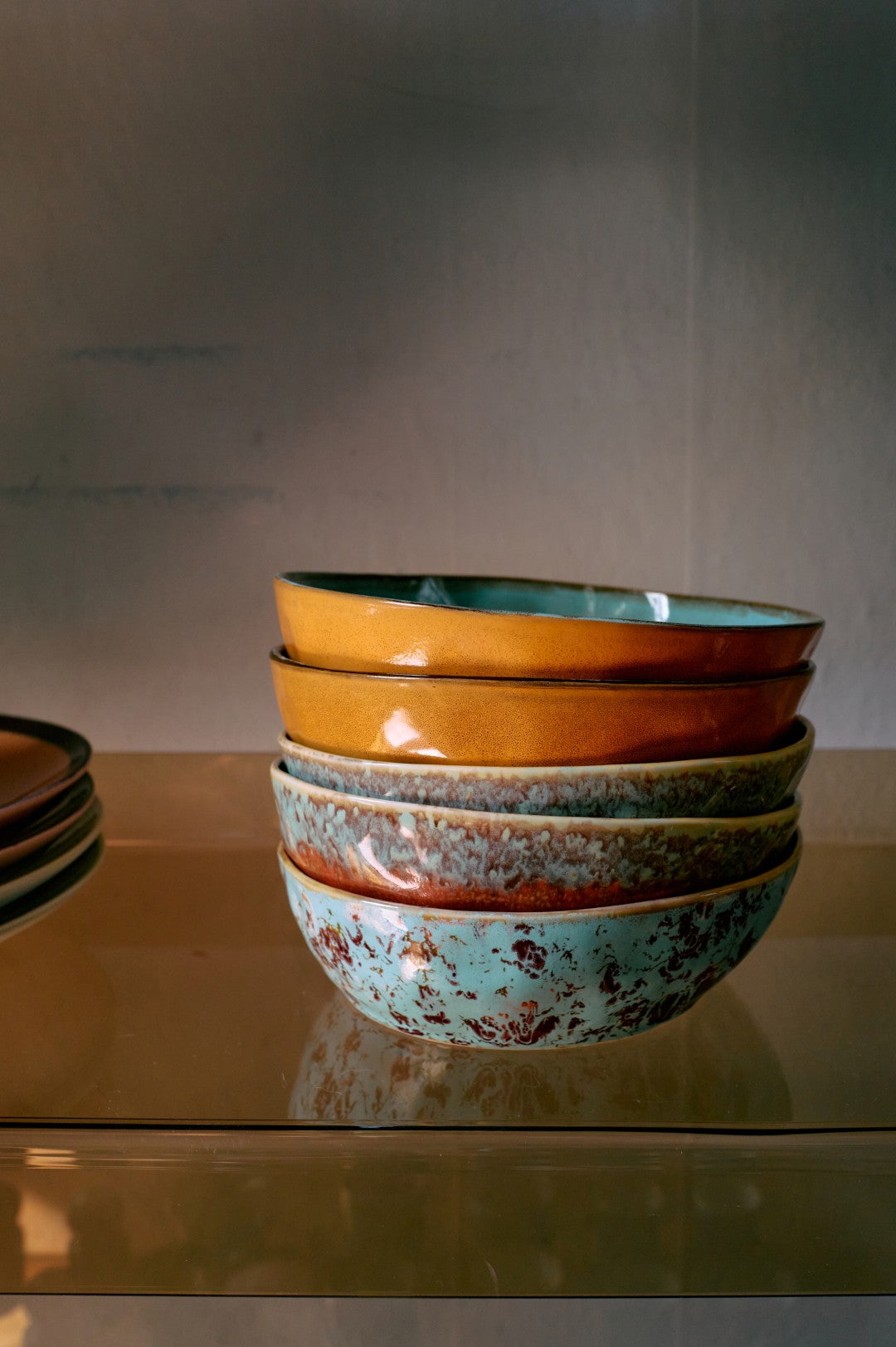 Stack of colorful ceramic bowls on a reflective surface with a neutral background
