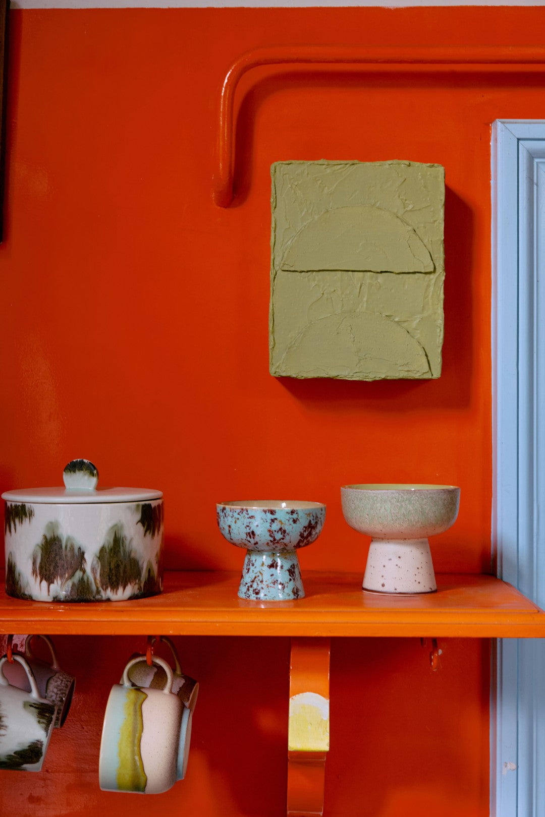 Decorative shelf with ceramic items against an orange wall