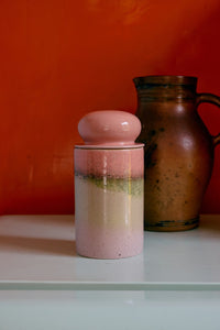 Ceramic jar with a pink lid on a white surface against an orange wall