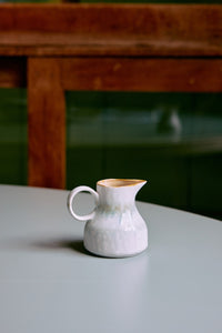 White ceramic pitcher on a light surface with a blurred background