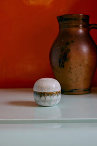 Small ceramic container with lid on a white surface against an orange wall