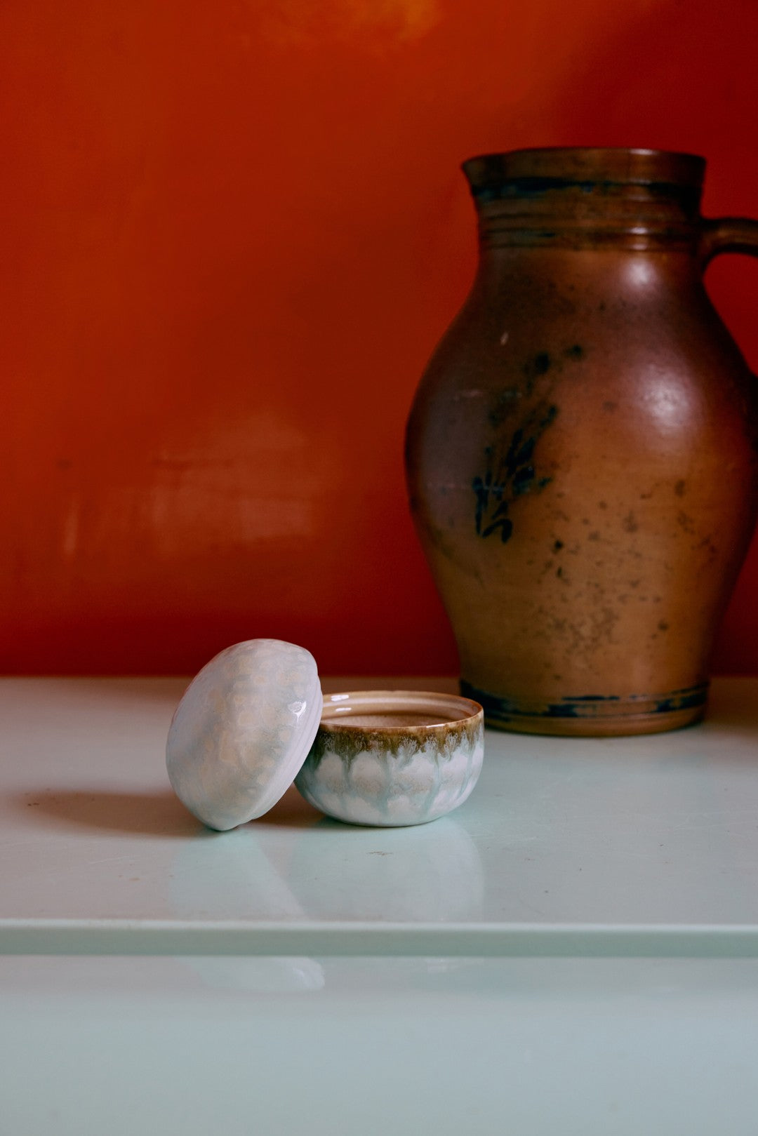Ceramic jar and bowls on a white surface with an orange wall background