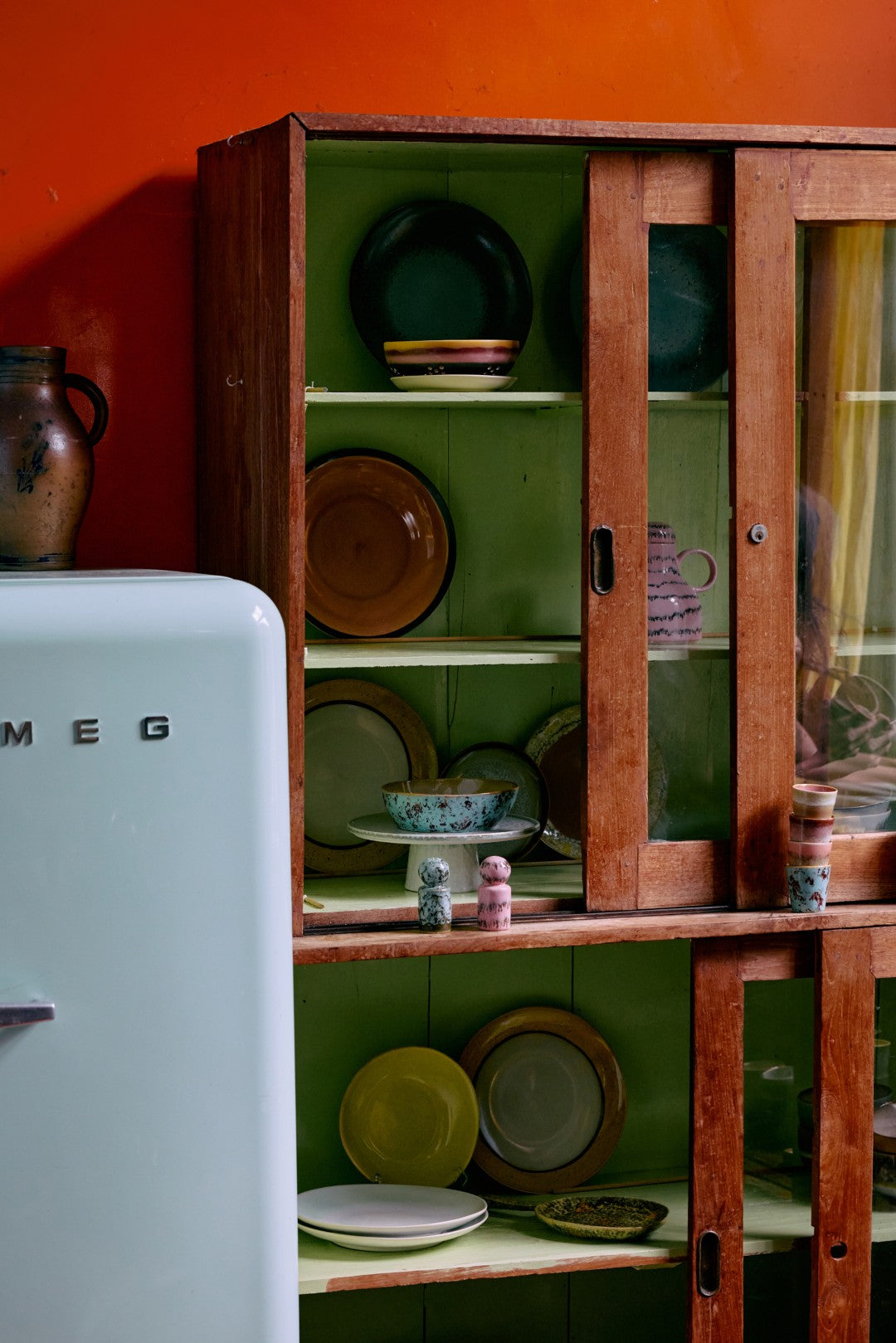 Vintage Smeg refrigerator next to a wooden cabinet with green interior displaying plates and bowls.