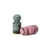 Two ceramic shakers, one green and one pink, on a white background