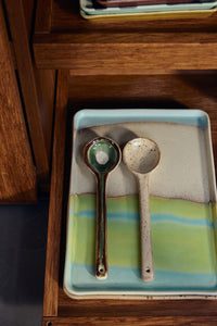 Two ceramic spoons on a rectangular plate with a wooden surface in the background