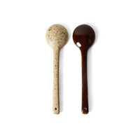Two wooden spoons, one speckled beige and the other dark brown, on a white background.
